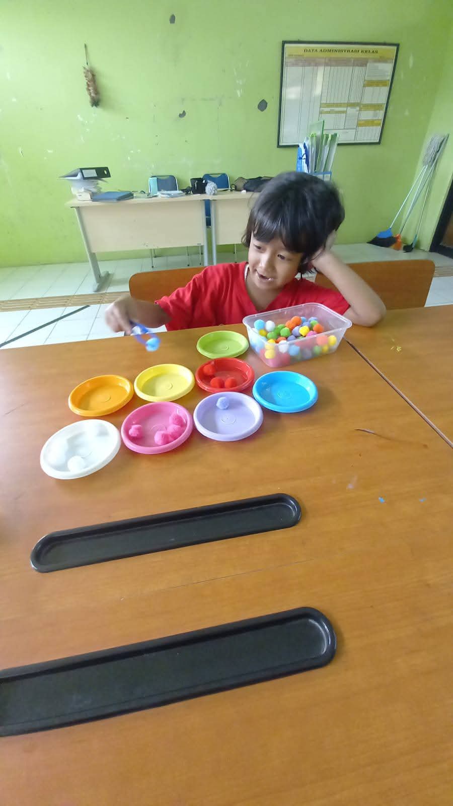 Anak mengelompokkan bola warna ke piring warna
